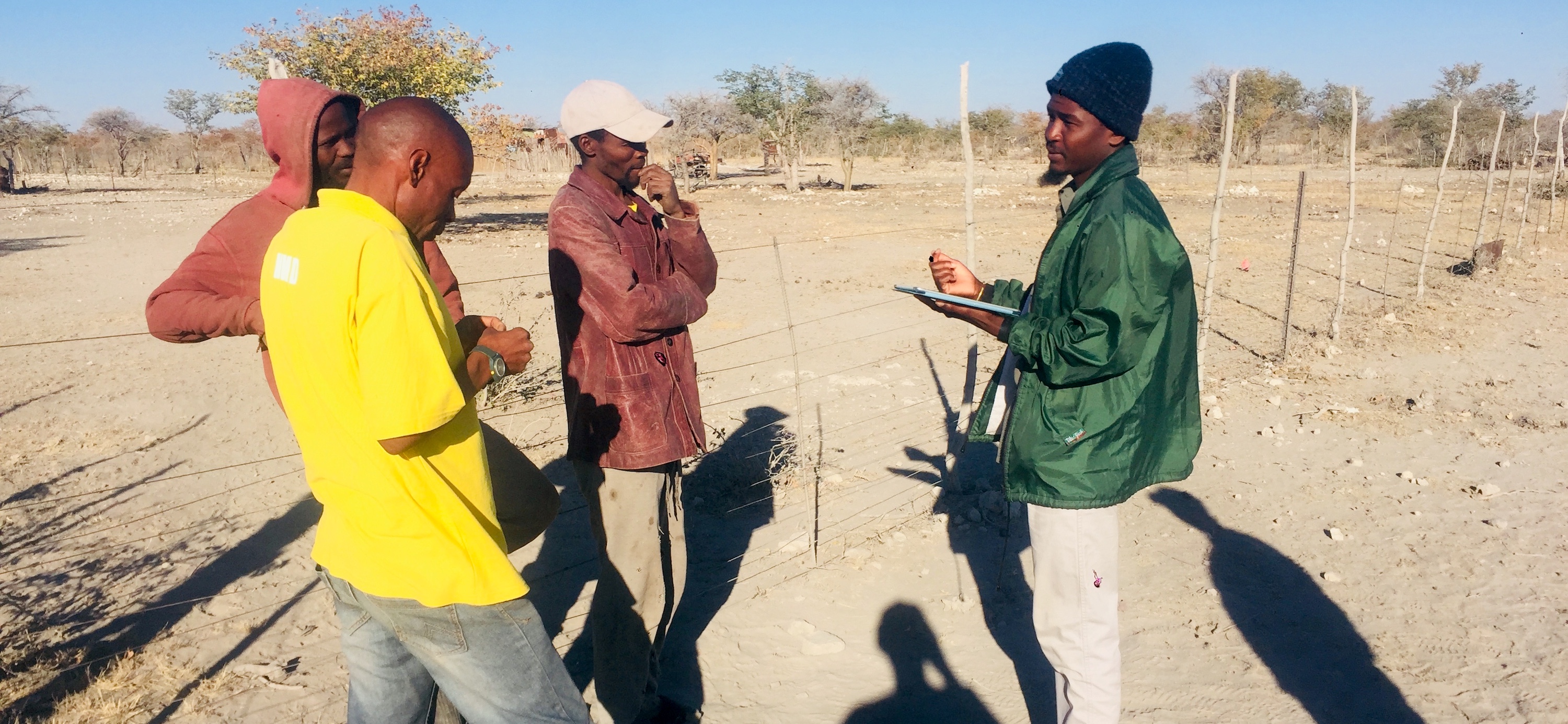 A group of men standing next to a kraal, while one (the author) takes notes.