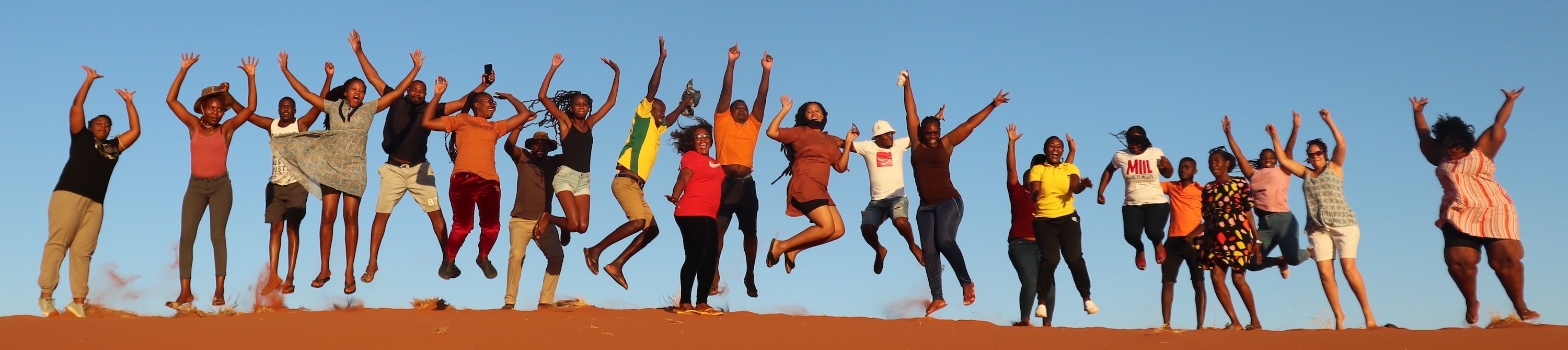 A long line of teachers jumping for joy on top of a sand dune.