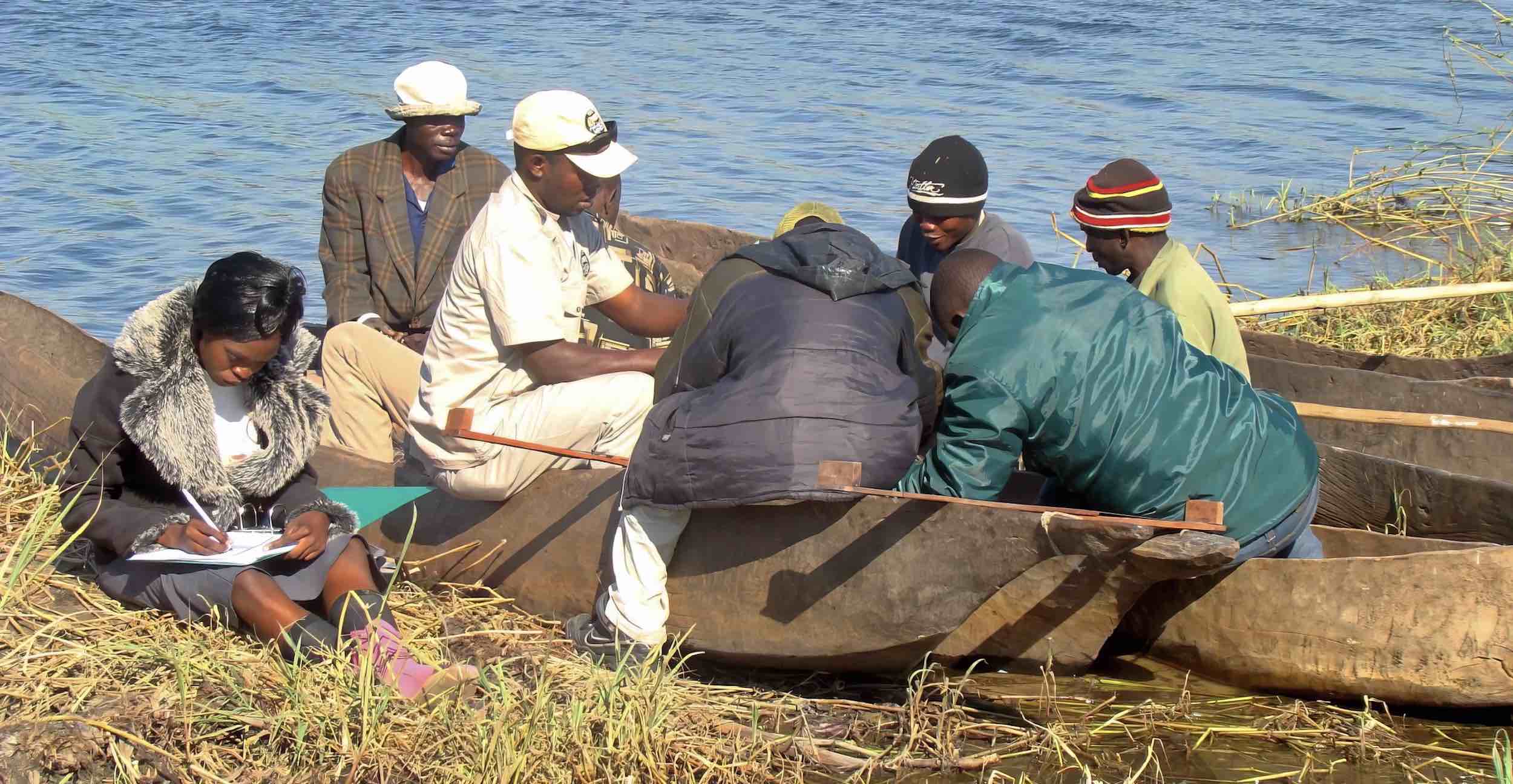 A woman records details on a clipboard, while a group of men look at the contents of a small boat.